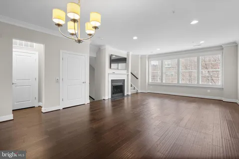 a view of an empty room with wooden floor and a kitchen