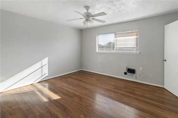 an empty room with wooden floor a ceiling fan and windows
