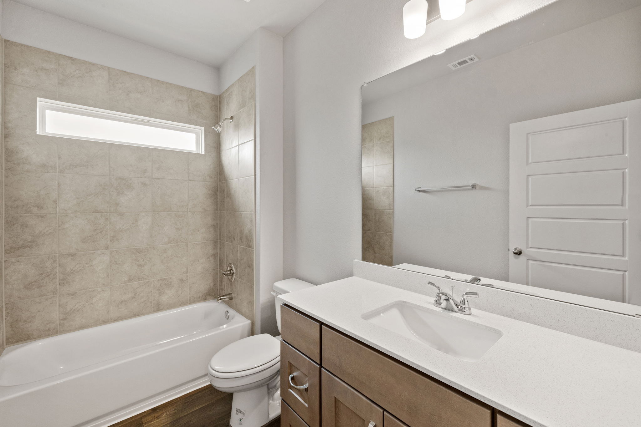 2460 Winding Creek Road Kyle, TX 78640 - Photo 16 of 20 A well-appointed bathroom features a sleek vanity, tiled shower with a bathtub, and wood plank flooring.