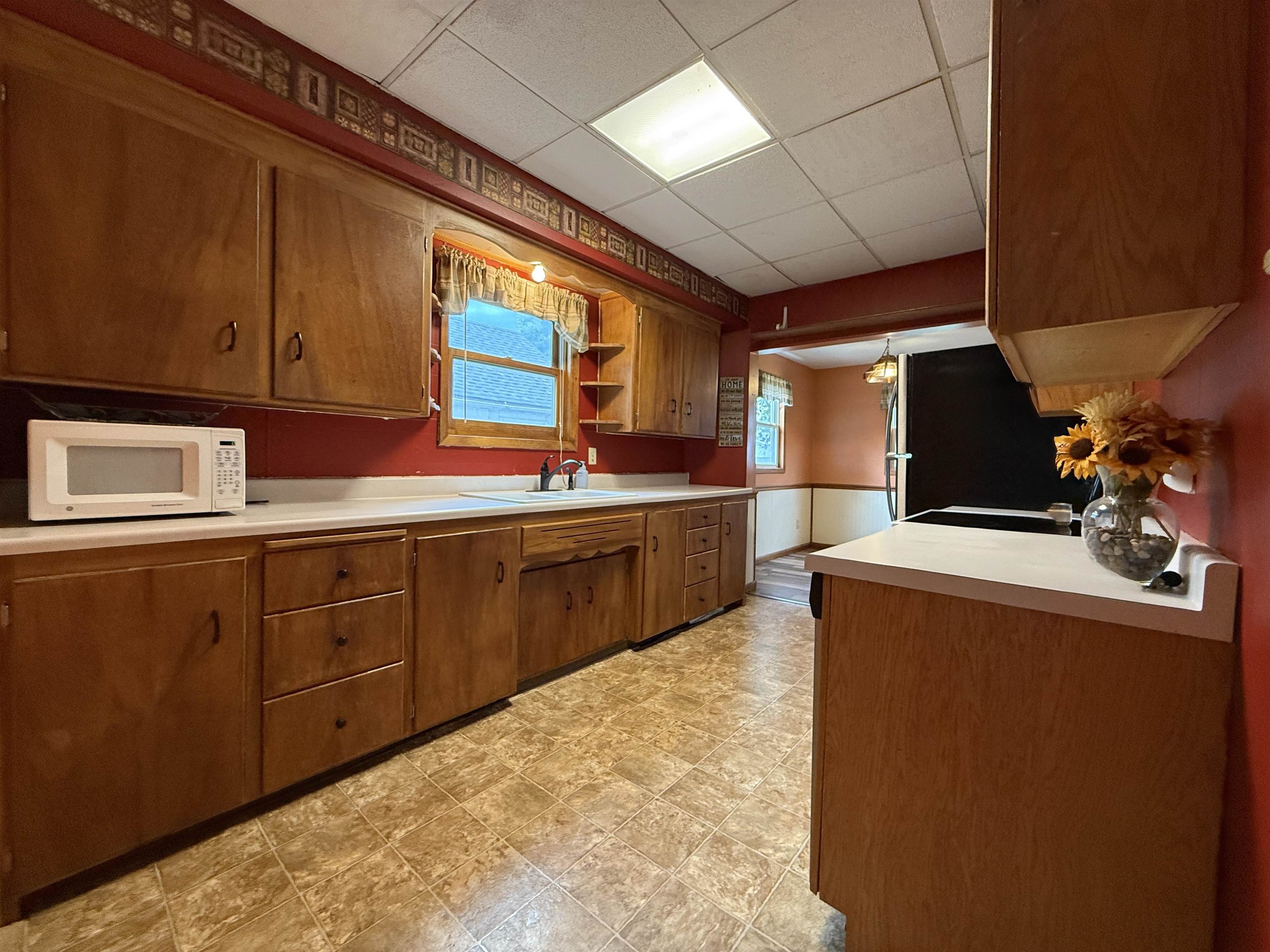 809 16th Street North Virginia, MN 55792 - Photo 19 of 44 Kitchen featuring a drop ceiling, brown cabinets, light countertops, white microwave, and open shelves