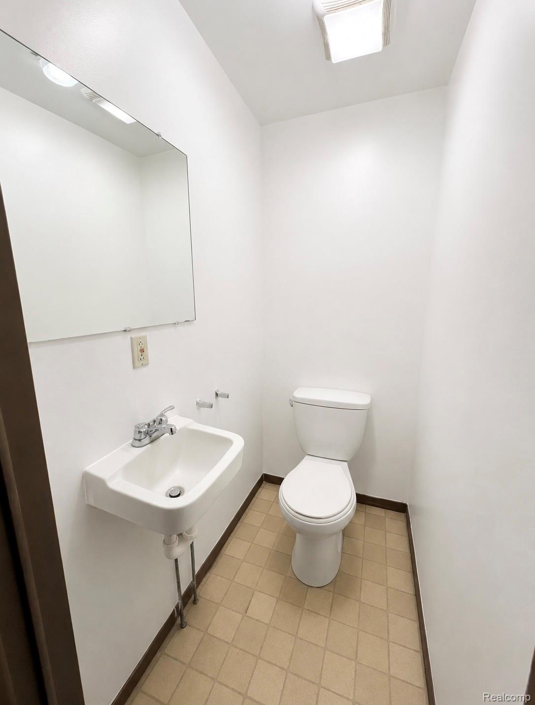 140 Larson Road Attica, MI 48412 - Photo 33 of 41 Wall-mounted sink with chrome fixtures, mirror with integrated lighting, white toilet, and neutral-toned tile flooring