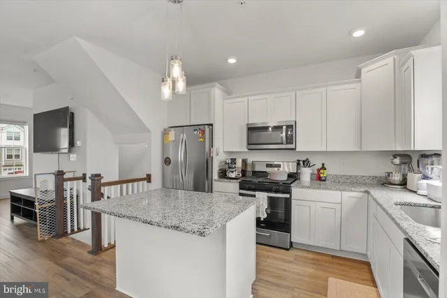 a kitchen with stainless steel appliances kitchen island granite countertop a refrigerator oven a sink dishwasher a dining table and chairs with wooden floor
