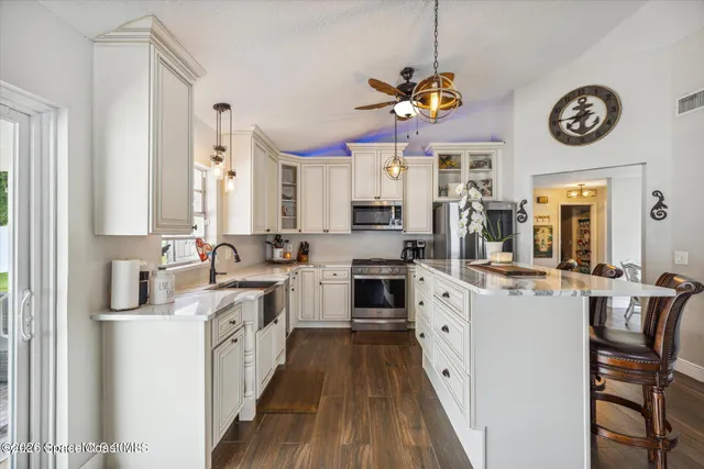 a large kitchen with a large island with stainless steel appliances granite countertop a stove a sink dishwasher and white cabinets with wooden floor