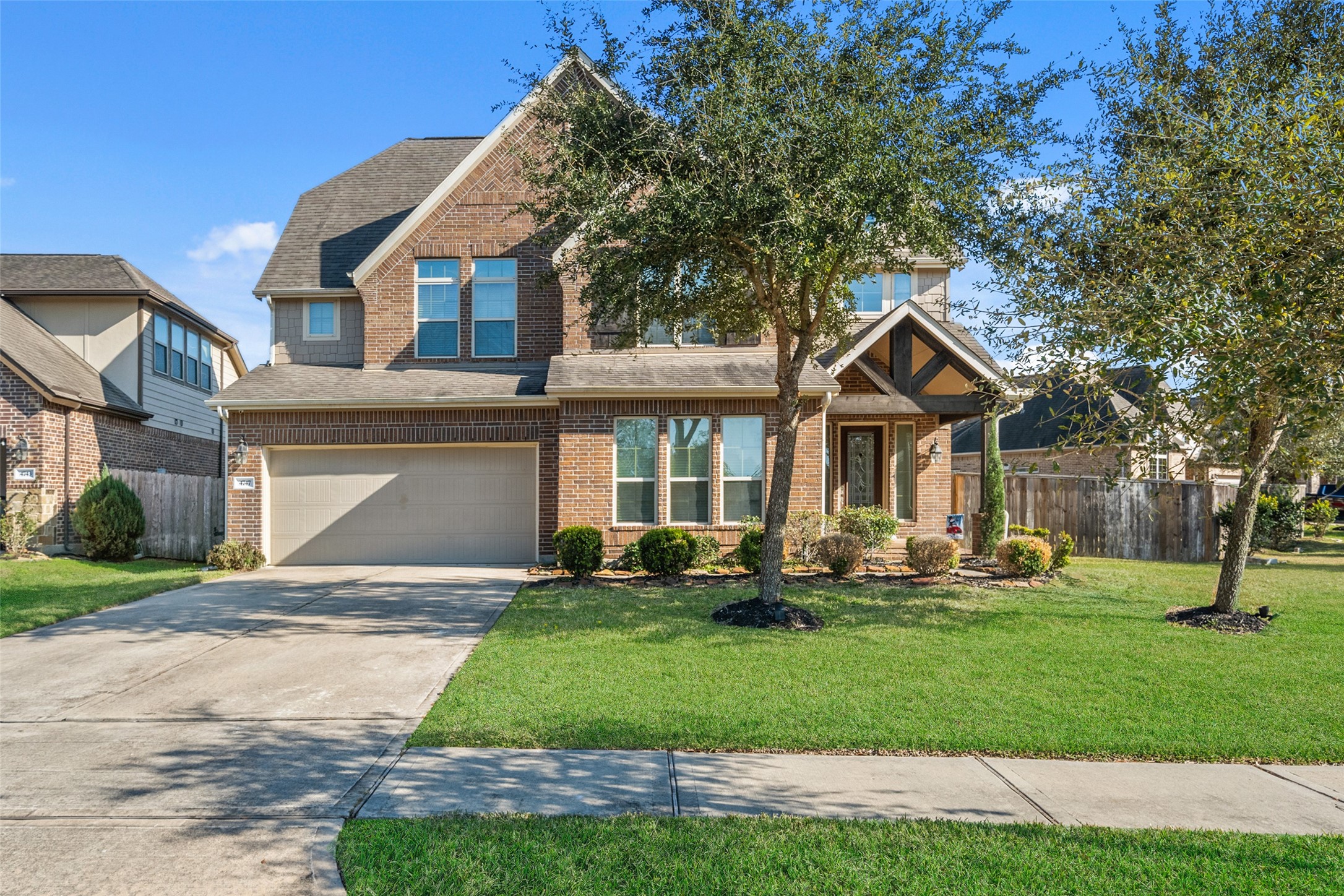 Charming two-story brick home with a gabled roof, featuring a spacious two-car garage and a well-maintained front yard with mature trees and shrubs. Ideal for family living in a suburban neighborhood.