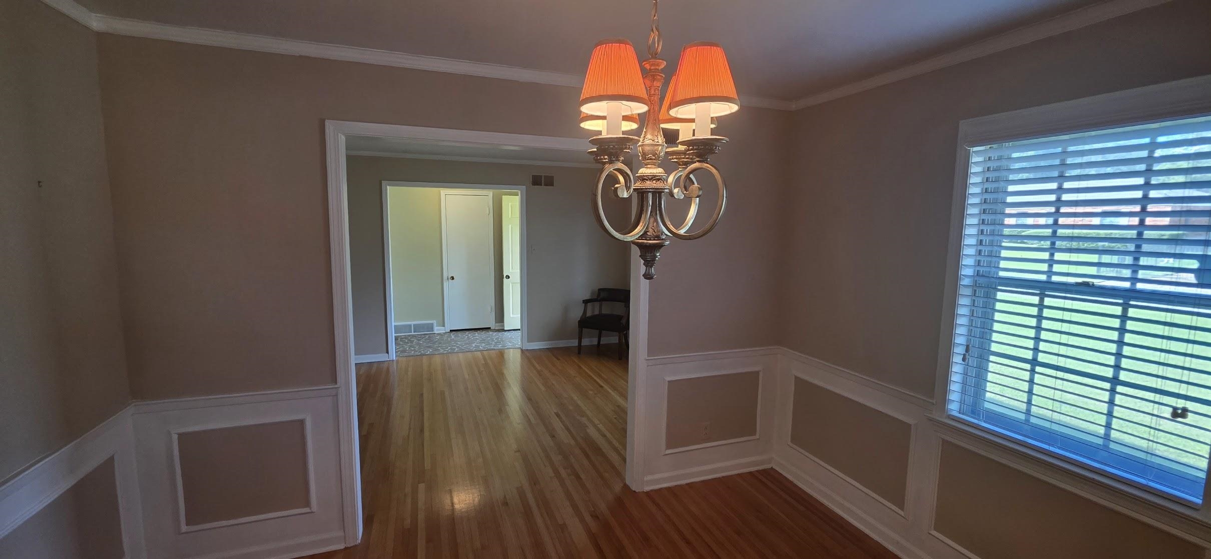 523 Shofner Avenue Memphis, TN 38109 - Photo 3 of 12 Unfurnished dining area with a decorative wall, a wainscoted wall, a chandelier, crown molding, and dark wood-style floors