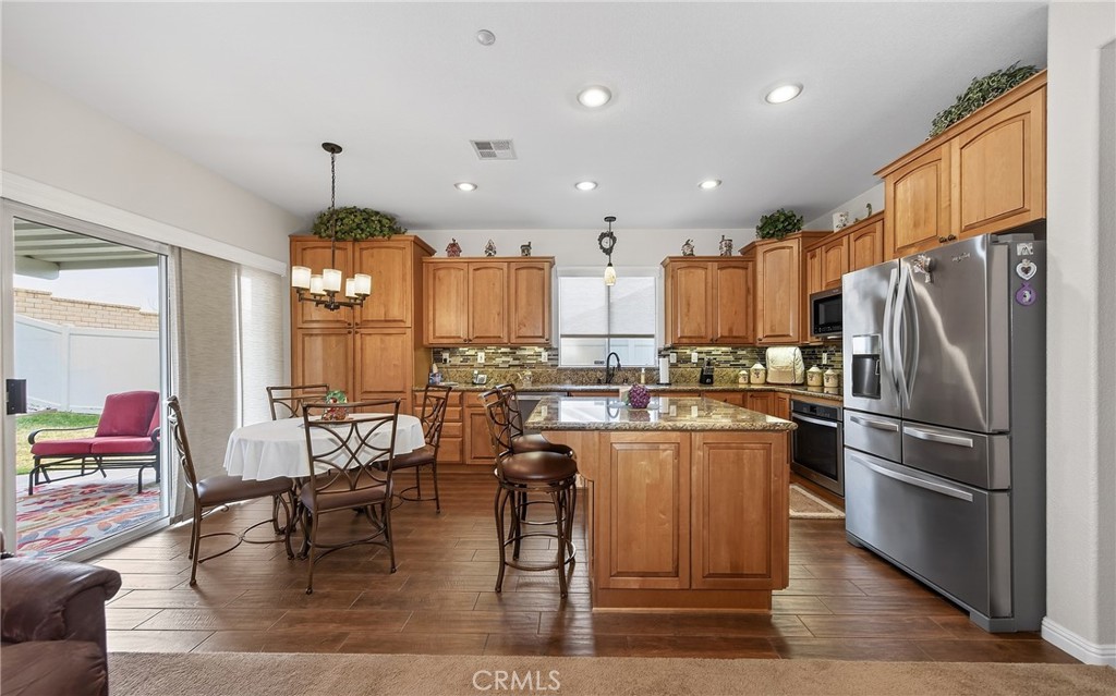 7619 Vista Rio Road Highland, CA 92346 - Photo 12 of 25 a kitchen with stainless steel appliances kitchen island granite countertop a stove a refrigerator a stove a dining table and chairs with wooden floor