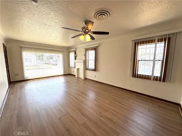 an empty room with wooden floor chandelier fan and windows