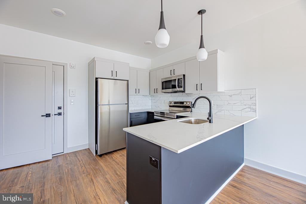 5001 Umbria Street, Unit U310 Philadelphia, PA 19128 - Photo 3 of 10 a kitchen with stainless steel appliances a sink a stove a refrigerator a center island with wooden floor and cabinets