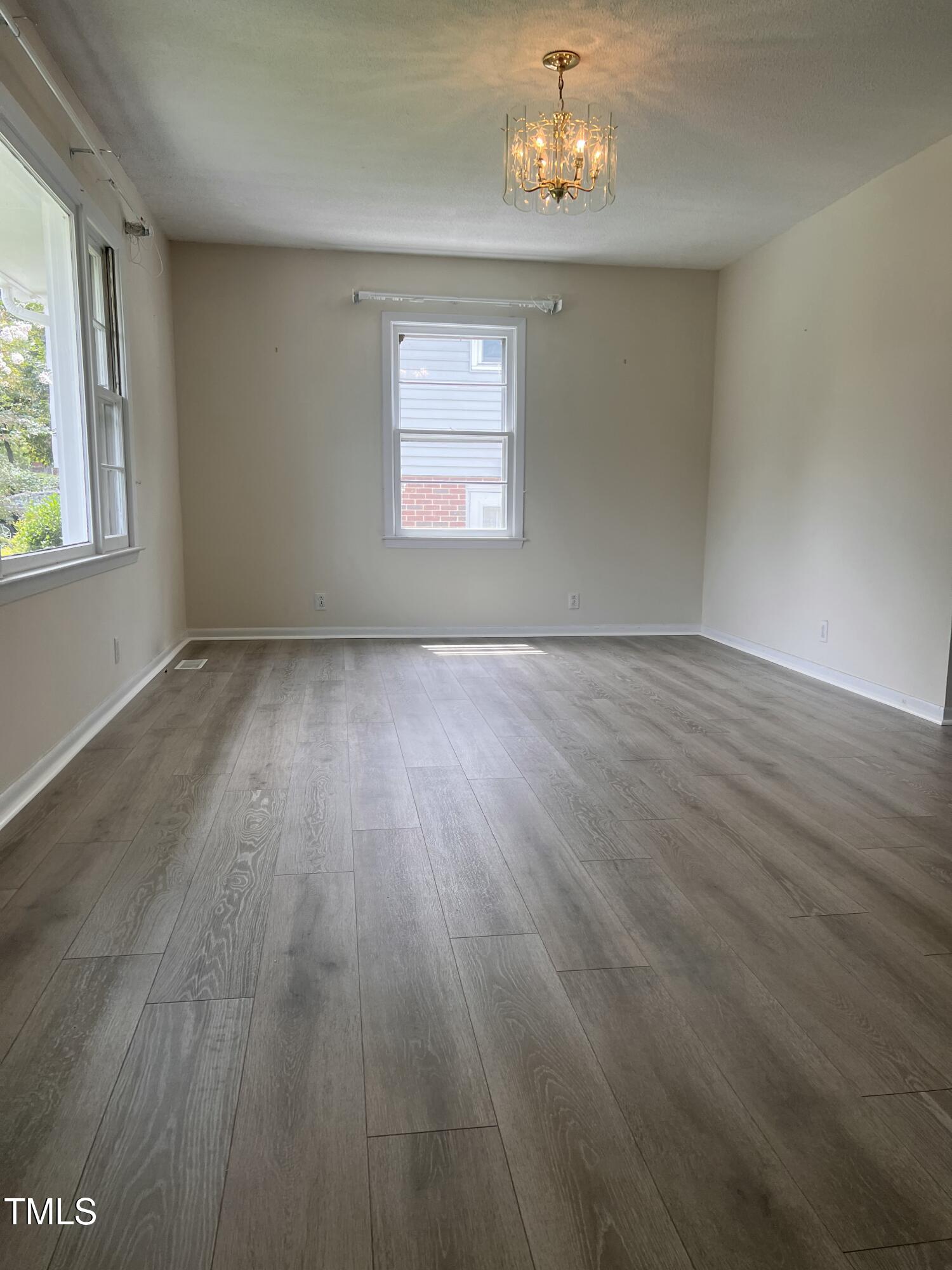 1517 Westchester Road Raleigh, NC 27610 - Photo 6 of 13 an empty room with wooden floor chandelier and windows