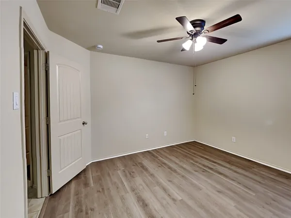 an empty room with a chandelier fan and wooden floor