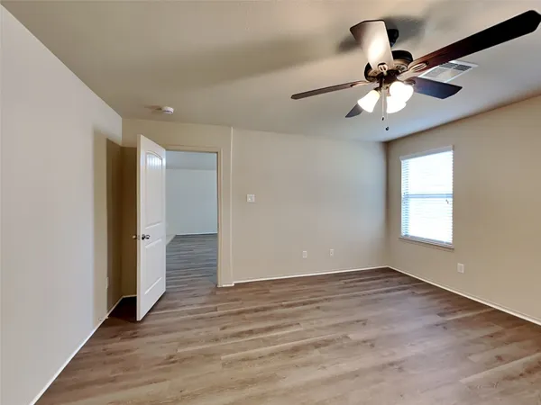 a view of an empty room with wooden floor and a ceiling fan
