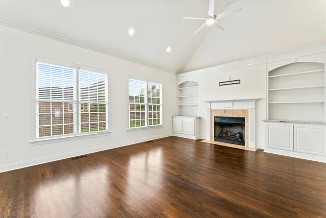 an empty room with wooden floor fireplace and windows