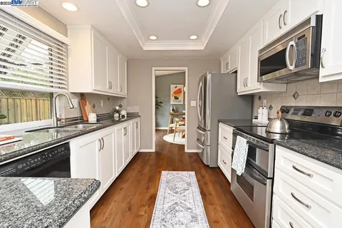 a kitchen with stainless steel appliances granite countertop a refrigerator a stove top oven a sink dishwasher and white cabinets