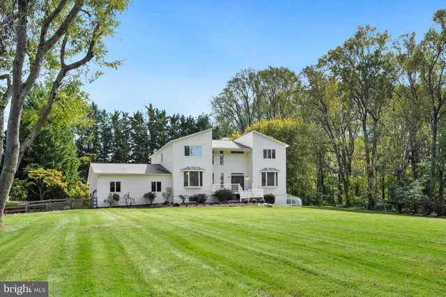 a view of a white house in front of a big yard with large trees