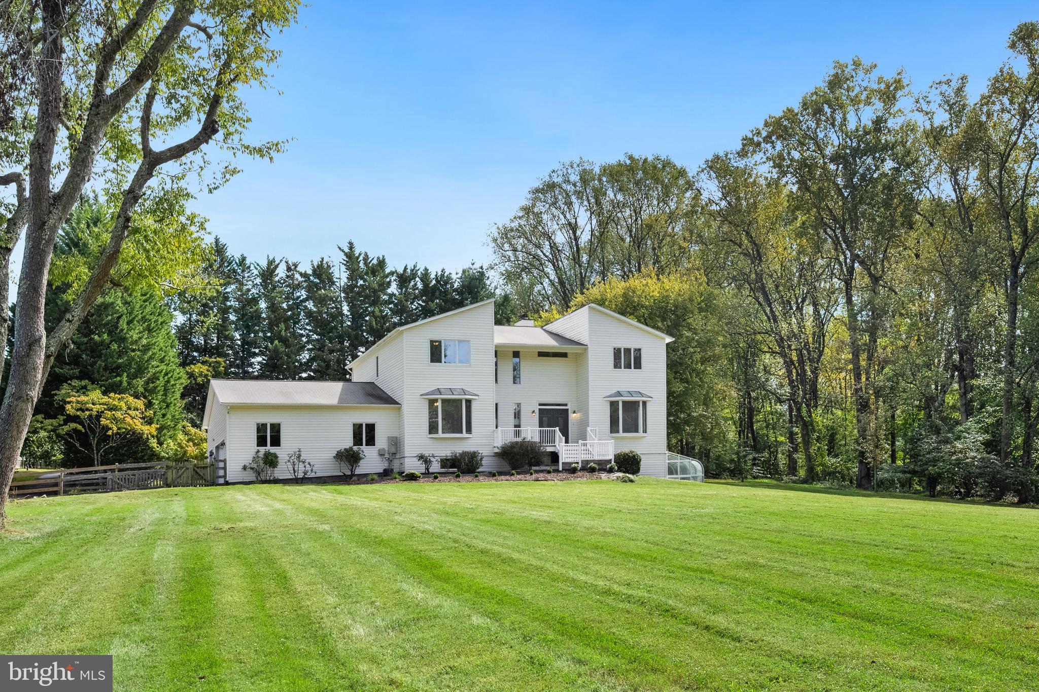 a view of a white house in front of a big yard with large trees