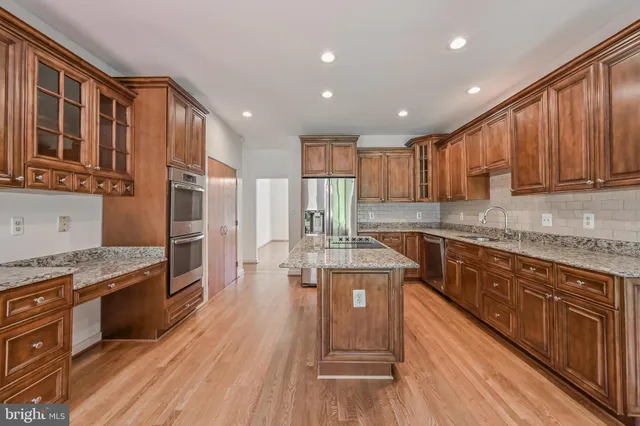 a kitchen with stainless steel appliances granite countertop a stove a sink dishwasher a refrigerator and wooden cabinets with wooden floor