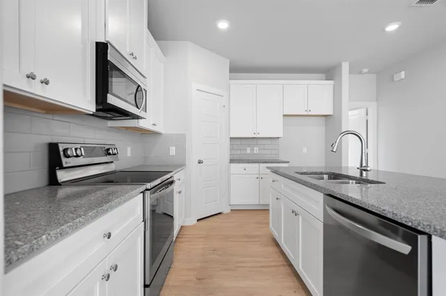 a kitchen with stainless steel appliances granite countertop a stove top oven a sink a refrigerator and white cabinets
