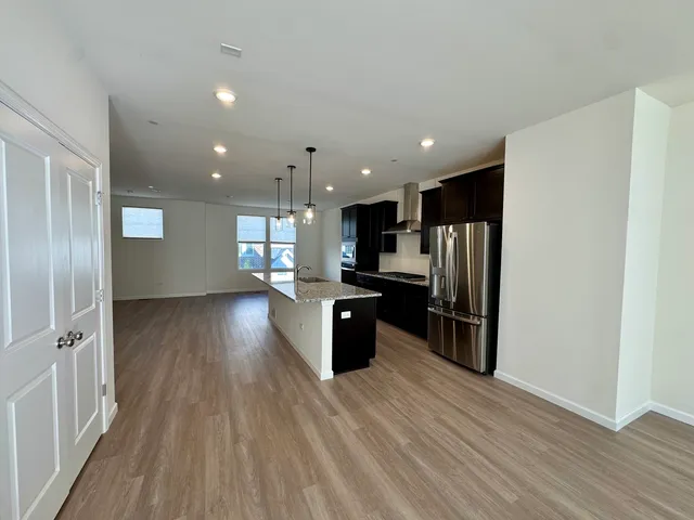 a kitchen with stainless steel appliances kitchen island granite countertop a refrigerator and a wooden floors