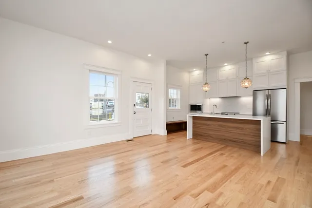 a view of kitchen with kitchen island a sink wooden floor white stainless steel appliances and cabinets