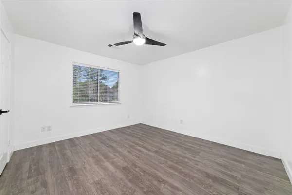 an empty room with wooden floor ceiling fan and windows