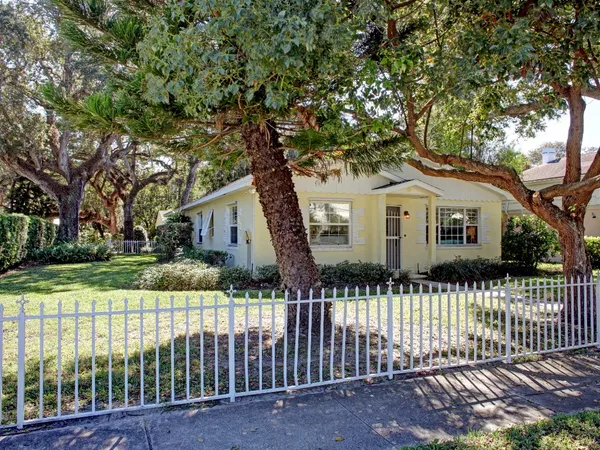 a white house that has a tree in front of it with wooden fence