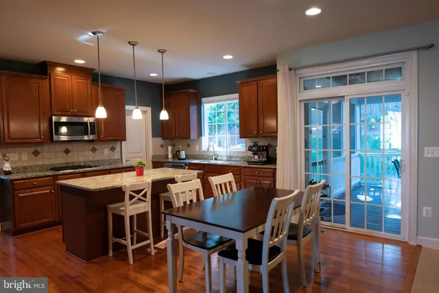 a kitchen with stainless steel appliances granite countertop a stove top oven a refrigerator a sink and a dining table with wooden floor