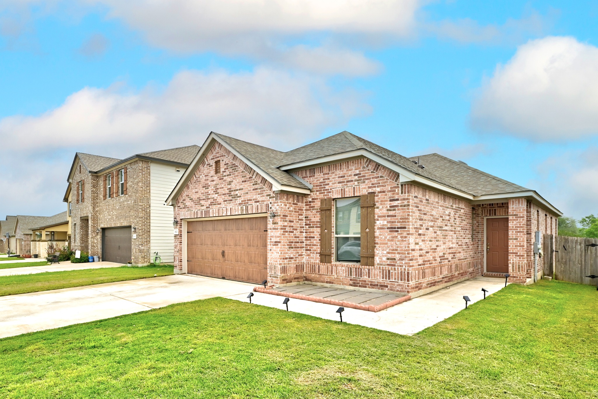 1621 Dragonfly Loop Bastrop, TX 78602 - Photo 4 of 27 Brick facade residence featuring a single-car garage, wood-look garage door, and a paved front patio