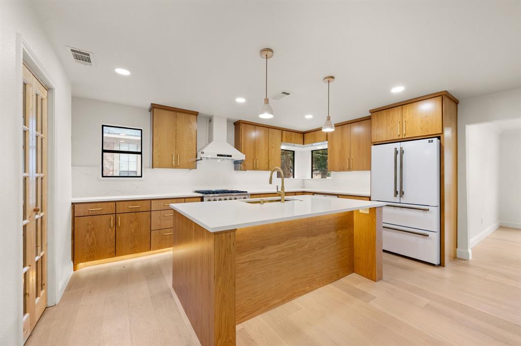 6403 Genstar Lane Dallas, TX 75252 - Photo 11 of 34 Spacious kitchen featuring an island with under-cabinet- and toekick lighting, light wood-finish flooring, white countertops, built-in stainless steel appliances, and natural wood cabinetry