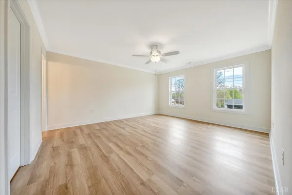 an empty room with wooden floor chandelier fan and windows