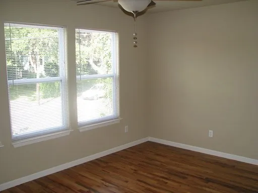 a view of an empty room with wooden floor and a window