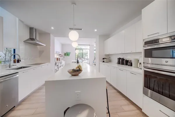 a large white kitchen with lots of counter top space a sink stainless steel appliances and cabinets