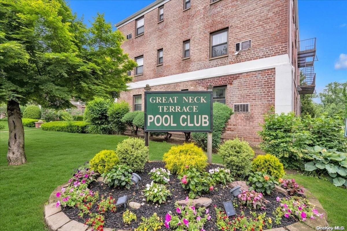 a sign that is sitting in front of a brick house with a big yard and potted plants
