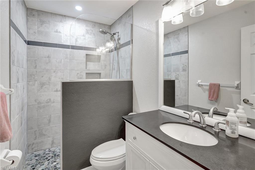 3520 2nd Avenue Northeast Naples, FL 34120 - Photo 23 of 39 a bathroom with a granite countertop sink a toilet a mirror and shower