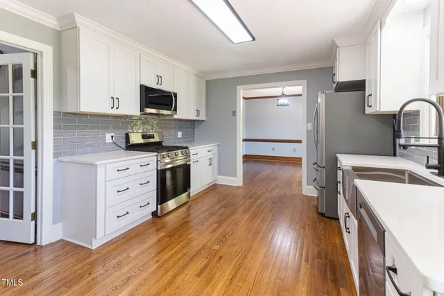 a kitchen with stainless steel appliances a stove top oven a sink dishwasher and a refrigerator with wooden floor