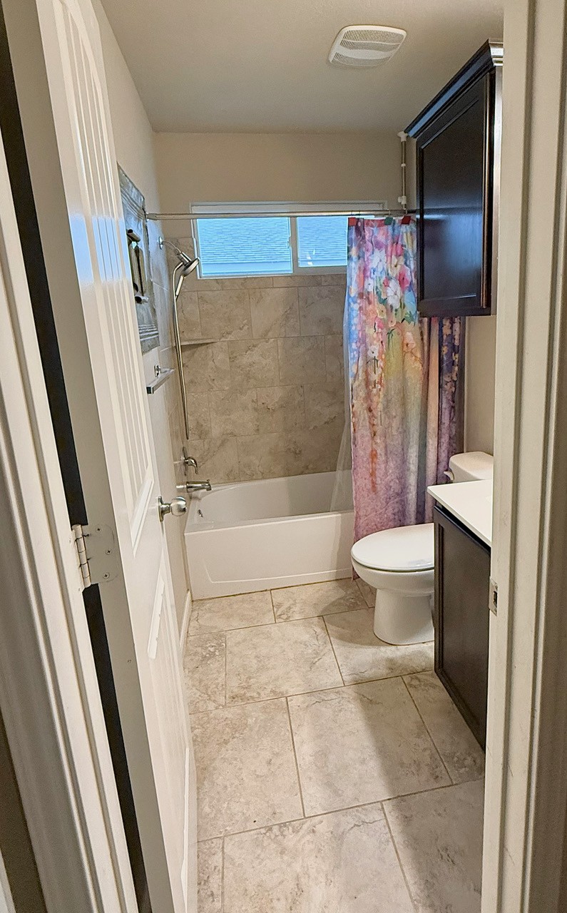 930 Pumpkin Ridge New Braunfels, TX 78130 - Photo 17 of 32 Bathroom featuring a full tub and shower combination with tile surround, a single vanity with a solid surface countertop, a wall-mounted cabinet, and large-format tile flooring