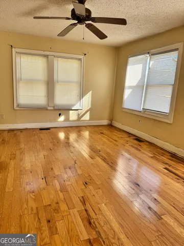 an empty room with wooden floor fan and windows