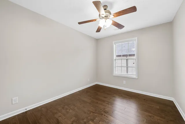 an empty room with wooden floor ceiling fan and windows