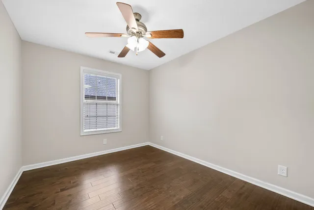 an empty room with wooden floor chandelier fan and windows