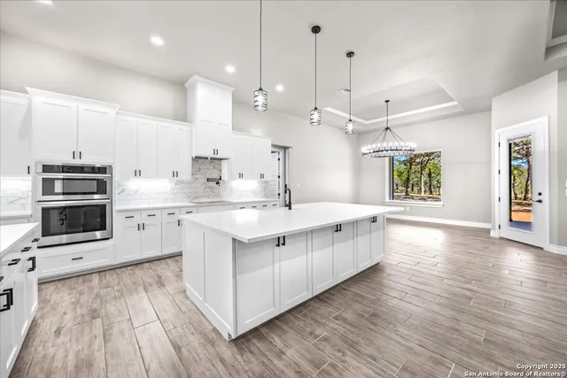 a large white kitchen with a large counter top a sink stainless steel appliances and cabinets