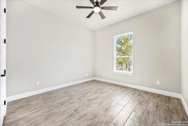 an empty room with wooden floor windows and fan
