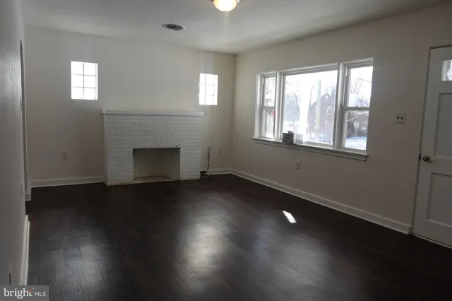 an empty room with wooden floor fireplace and windows
