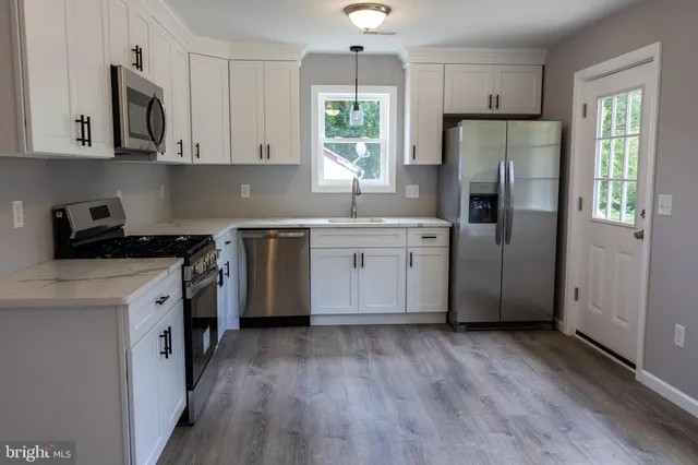 a kitchen with stainless steel appliances granite countertop a refrigerator a sink dishwasher a stove and white countertops with wooden floor