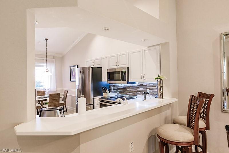 8135 Celeste Drive, Unit 4218 Naples, FL 34113 - Photo 14 of 37 Kitchen featuring white cabinetry, lofted ceiling, a breakfast bar area, stainless steel appliances, and decorative light fixtures
