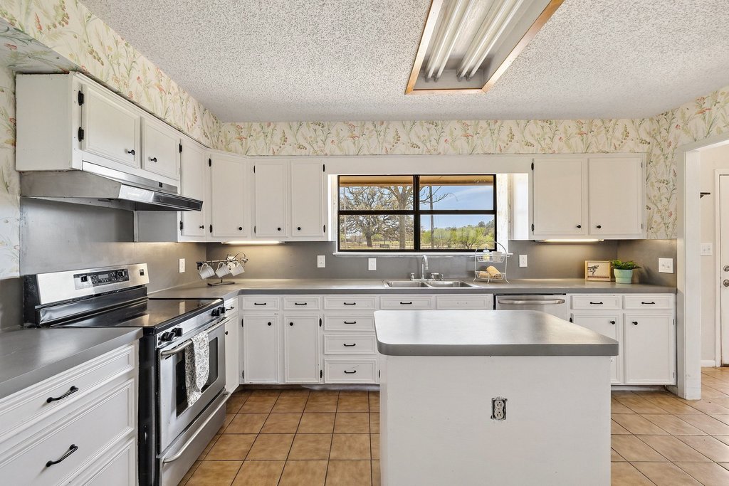3410 West Ranch Road 152 Llano, TX 78643 - Photo 12 of 36 Kitchen featuring wallpapered walls, stainless steel appliances, white cabinetry, a textured ceiling, and a kitchen island