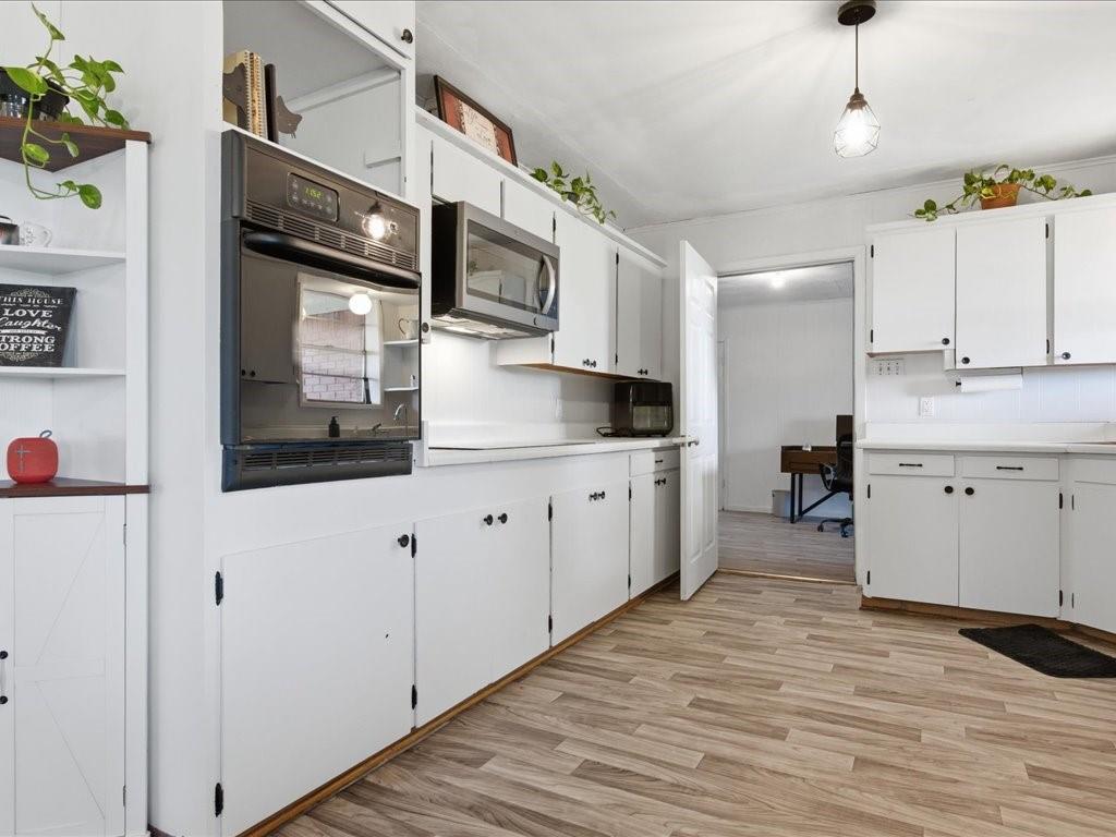 1085 Duke Road Kennard, TX 75847 - Photo 12 of 40 Kitchen featuring extensive white cabinetry with black hardware, wood-finish flooring, built-in wall oven, and microwave