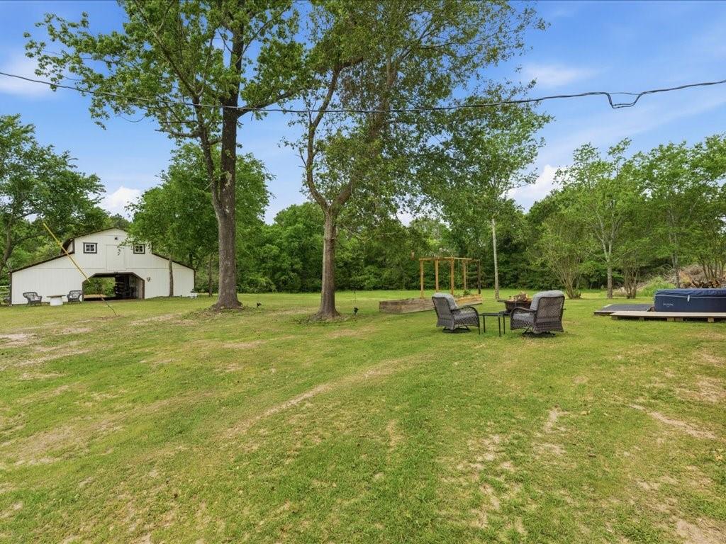 1085 Duke Road Kennard, TX 75847 - Photo 26 of 40 Expansive green space featuring a white barn structure with open bays, mature trees, and a wooden pergola