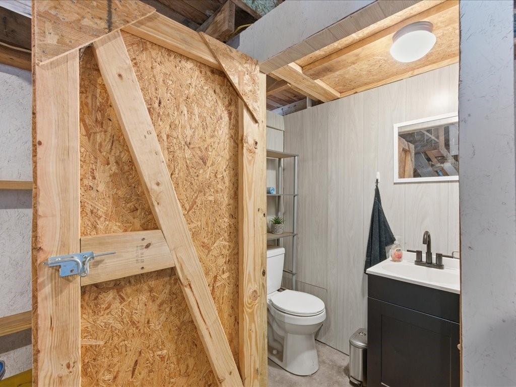 1085 Duke Road Kennard, TX 75847 - Photo 31 of 40 Compact bathroom featuring a white toilet, black vanity with a white countertop and dark-finish faucet, light wood-look wall paneling, and a flush-mount ceiling light