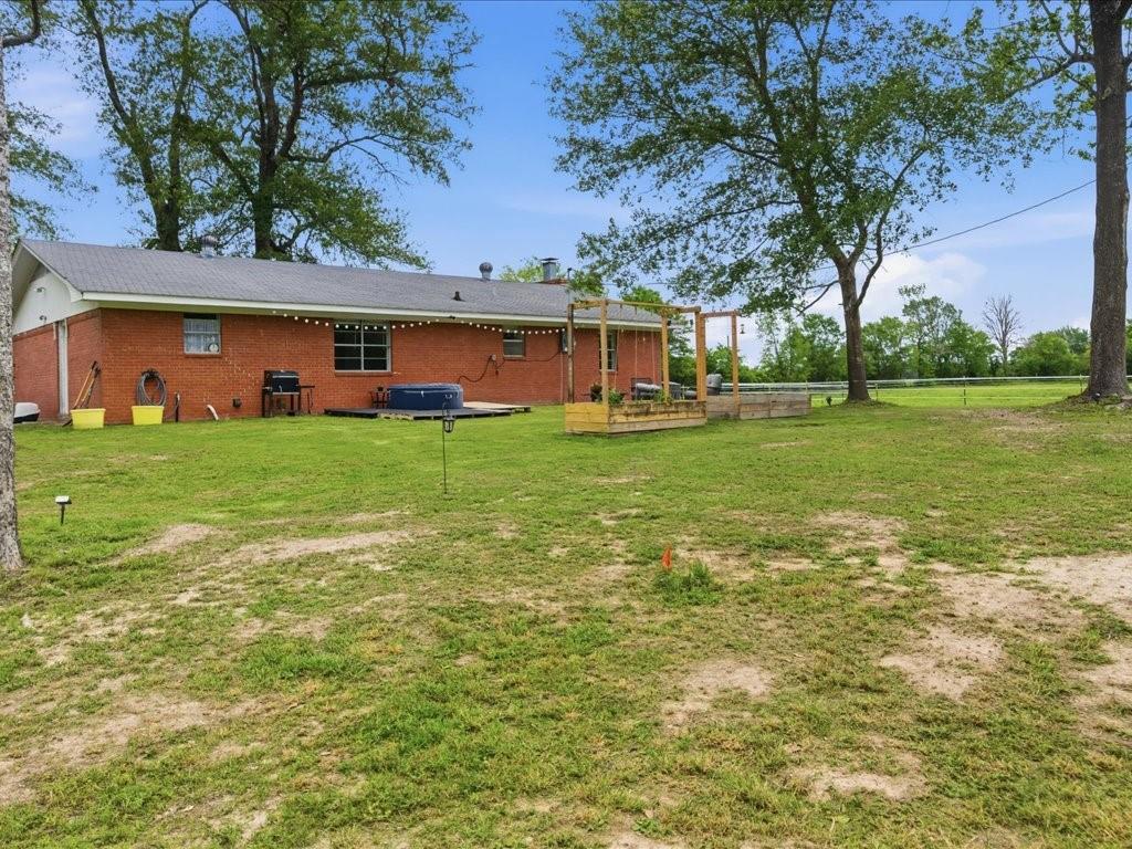 1085 Duke Road Kennard, TX 75847 - Photo 39 of 40 Expansive backyard featuring a red brick exterior, a raised wooden deck with an overhead trellis, mature trees, and a substantial green area
