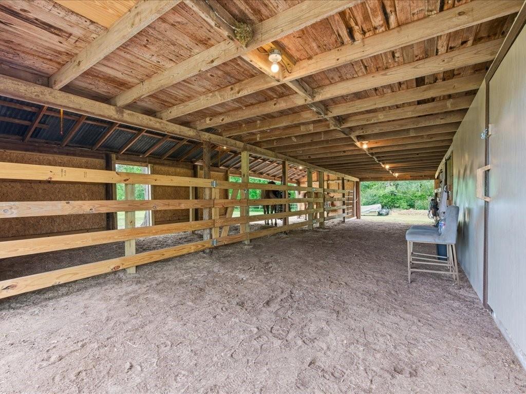 1085 Duke Road Kennard, TX 75847 - Photo 6 of 40 Covered barn structure featuring a wood-beam ceiling, exposed wood framing, interior lighting, and partitioned stalls with wooden fencing