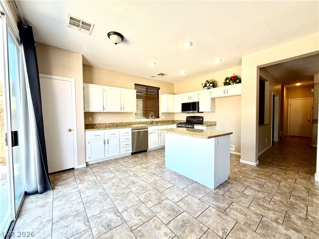 3936 Gold Point Street Las Vegas, NV 89129 - Photo 4 of 23 A functional kitchen with white cabinetry and an island offers a delightful culinary space.